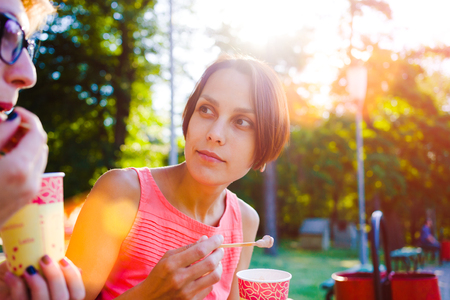 girl eats ice cream with a disposable Cup, a woman with a glass in hand laughing and smiling.の写真素材