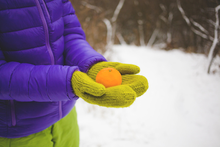 female hands in warm green mittens holding a Mandarin on a background of snow.の写真素材