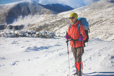 girl with backpack walking on snow in the mountains and mountain climbing during the winter holidays.の写真素材