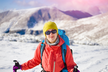 girl with backpack walking on snow in the mountains and mountain climbing during the winter holidays.の写真素材