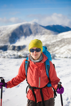 girl with backpack walking on snow in the mountains and mountain climbing during the winter holidays.の写真素材