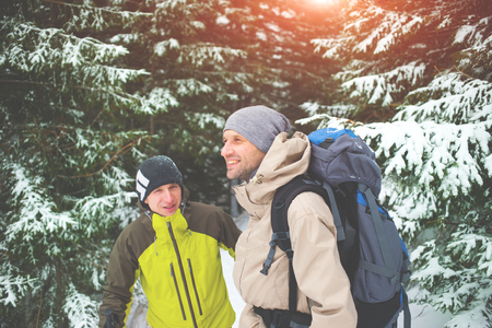 two friends with backpacks in the winter woods on a background of snow-covered fir trees, friends communicate in the winter forest.の写真素材