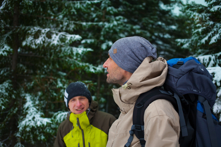 two friends with backpacks in the winter woods on a background of snow-covered fir trees, friends communicate in the winter forest.の写真素材