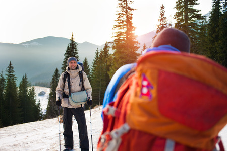 Man with backpack and trekking sticks is photographed on the background of snowy mountains.の写真素材