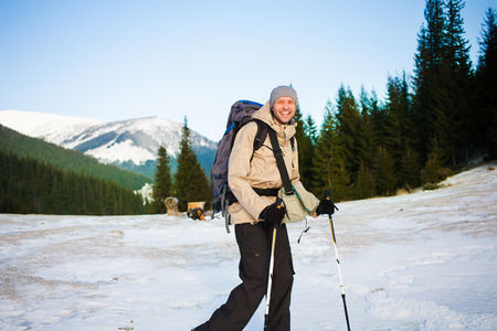 Man with backpack and trekking sticks is photographed on the background of snowy mountains.の写真素材