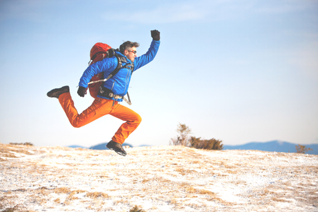 A climber with a backpack jumps on the background of snowy mountain and blue sky.の写真素材