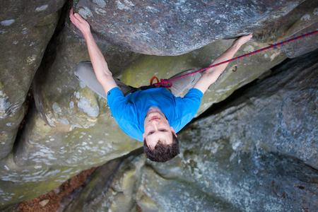 a young rock climber climbs the cliff, a man in a blue shirt climbs on the wall.の写真素材