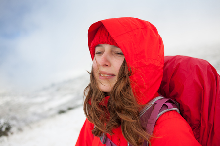 Portrait of a young woman with a backpack in the mountains, girl in a red cap on a background of snow-capped mountains, the wind blowing in the face of the girl.の写真素材