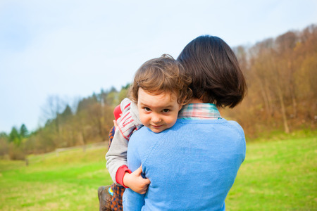 The mother carries the child in her arms, the baby lies in his mother's shoulder on a background of green field.の写真素材