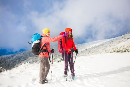 Two friends talk on the background of snow-capped mountain and beautiful sky with cloud. The woman points the way. Tourist choose the road.の写真素材