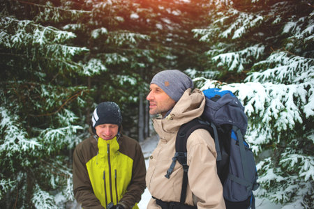 two friends with backpacks in the winter woods on a background of snow-covered fir trees, friends communicate in the winter forest.の写真素材