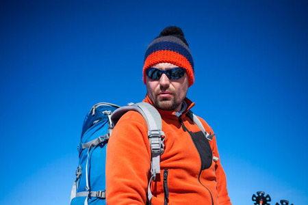 Portrait of climber in a knitted hat, a man with a backpack smiling against the blue sky.の写真素材