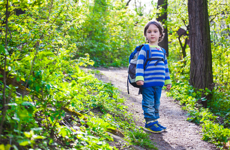 Little boy with backpack standing on forest trail. A child walks in the forest among the trees.の写真素材