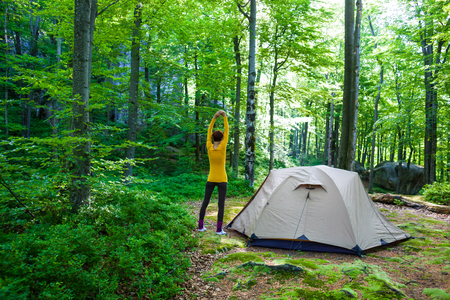 The girl is standing near the tent. Morning yoga in the forest after awakening.の写真素材