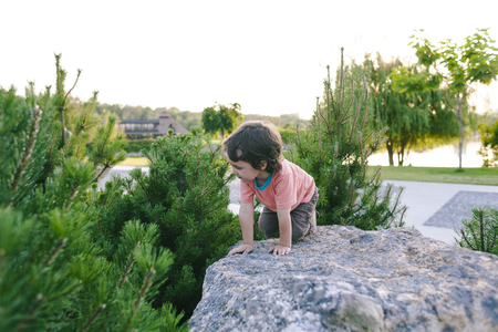 The little boy climbs on the stone. Activity in nature during the holidays. Sport activity.の写真素材