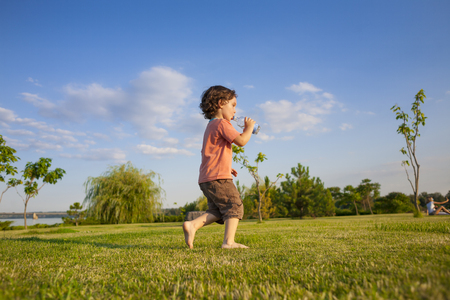 The child runs along the grass with a bottle of water in his hand, a fun vacation in nature.の写真素材