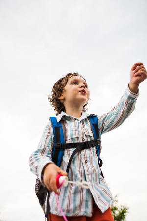 A boy with a backpack is playing with soap bubbles. A curly-haired child lets and catches soap bubbles in the park.の写真素材