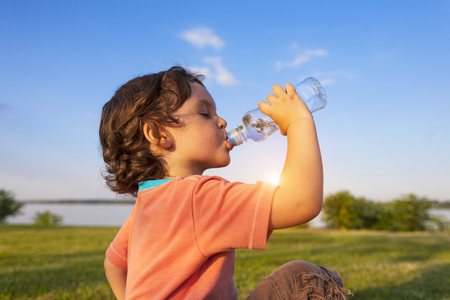 A child drinks water from a bottle while walking, baby health.の写真素材