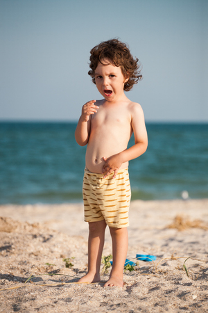 Crying boy on the beach. A small child is standing by the sea and crying. The kid is standing on the sandy beach.の写真素材