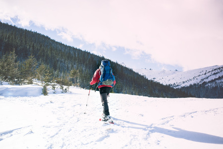 The tourist in snowshoes walks through the snow and carries a large backpack. Adventure of people in the mountains in winter.の写真素材