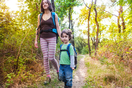 family on a hike through the forest in the autumn. travel with a child in the autumn park. a woman and a child with backpacks are walking along the path.の写真素材