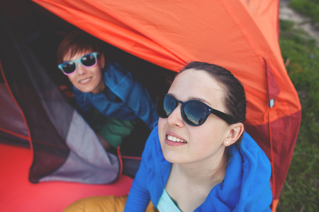 Two girls are sitting near the tent during the hike. Friends are resting in nature.の写真素材
