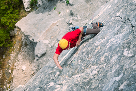 A rock climber in a hat on a rock. A man climbs the rock. Active lifestyle. Sports in nature. Overcoming a difficult climbing route.の写真素材