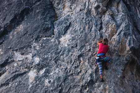 The girl climbs the rock. The climber trains on a natural relief. Extreme sport. Active recreation in nature. A woman overcomes a difficult climbing route.の写真素材