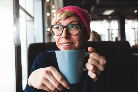 portrait of a girl in a pink hat with a mug of coffee. laugh and smile while meeting friends.の写真素材