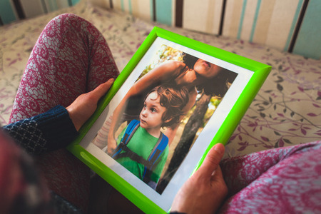 A woman looks at a photo of a boy. Mom holds a photo frame with a photograph of her son. A small child and memories.の写真素材