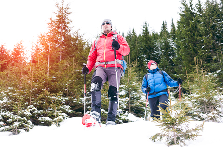 Two climbers in snowshoes are in the mountains in the winter against fir trees, climbing two men with backpacks. A climber with trekking sticks walks through the snow. Climbing in winter.の写真素材