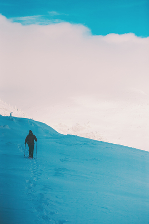 A man in snowshoes and trekking sticks in the mountains. Winter trip. Climbing of a climber against a beautiful sky with clouds. Active lifestyle. Climbing the mountain through the snow.の写真素材