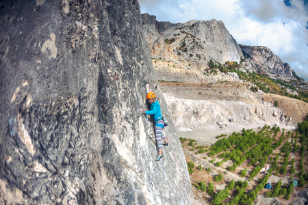 Rock climber on a rock. Girl climbs the rock on the background of a beautiful mountain landscape and the sky with clouds. Active lifestyle. Sports in nature. Overcoming a difficult climbing route.の写真素材