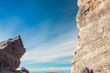 A rock climber on a rock on the background of the sea coast. The girl climbs the rock on the background of a beautiful mountain landscape and the sky with clouds. Active lifestyle. Sports in nature.の写真素材