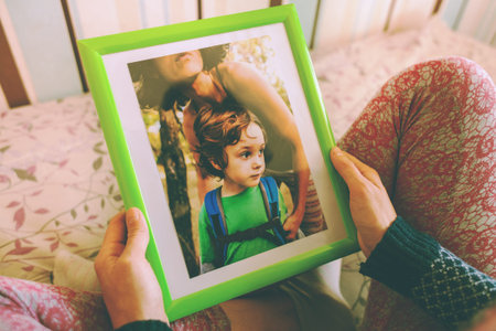 A woman looks at a photo of a boy. Mom holds a photo frame with a photograph of her son. A small child and memories.の写真素材