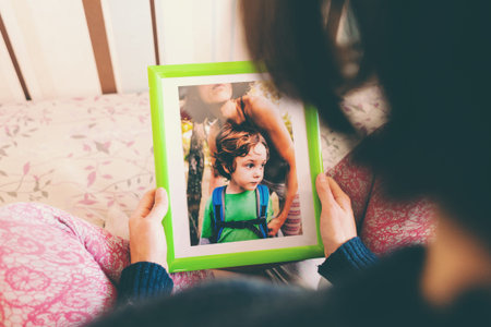 A woman looks at a photo of a boy. Mom holds a photo frame with a photograph of her son. A small child and memories.の写真素材