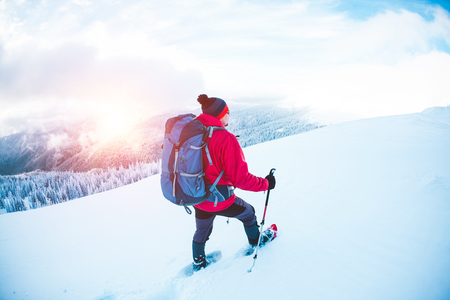 A man in snowshoes and trekking sticks in the mountains. Climbing the mountain through the snow.の写真素材
