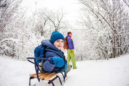 A woman is carrying a child on a sled. Mom walks with her son on the snow trail. Cheerful winter...