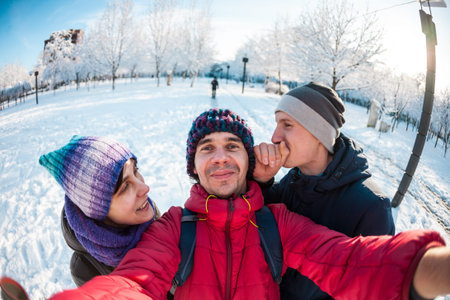 Friends on a winter walk. A girl and two men make faces on the camera. Selfi three friends. Merry...