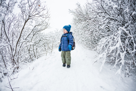The boy runs through the snow. A child with a backpack runs away from her mother on a forest path. Winter fun.の写真素材