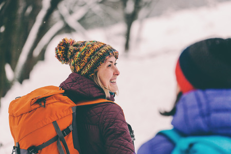 travel with a backpack in the woods in winter in the snow. two girls walk through the forest and laugh. conversation between two friends.の写真素材