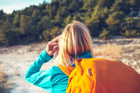 A girl with a backpack walks along the mountain path. A woman is walking along a stony road. Blonde...