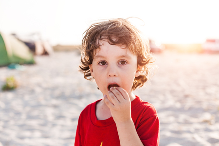 Portrait of a boy. Curly toddler eating. Child on the beach. The boy is resting on the sea coast.の写真素材