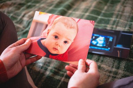 Photos of a small child. A woman looks at old photographs and remembers the events of the past. Nostalgic memories. Newborn baby on paper photos.の写真素材