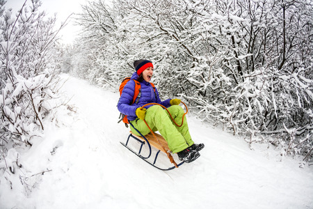 A girl on a sled rides from the mountain. Descent on a sleigh. Snow Hill. Cheerful winter vacations.の写真素材