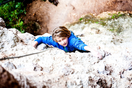The boy climbs the rock. The child is engaged in rock climbing on a natural relief. The sports kid actively spends time. Exercise in the fresh air.の写真素材