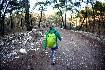 A woman with a backpack travels to beautiful places. Girl on the background of mountains. The blonde is walking along a stony path. A tourist walks along a forest trail.の写真素材