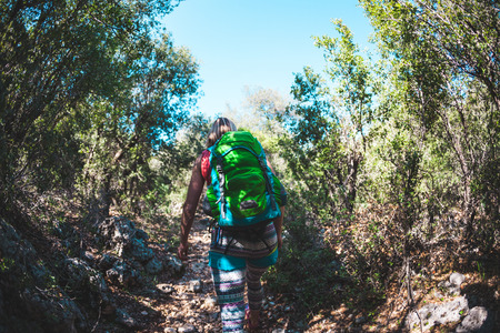 A woman with a backpack travels to beautiful places. Girl on the background of mountains. The blonde is walking along a stony path. A tourist walks along a forest trail.の写真素材