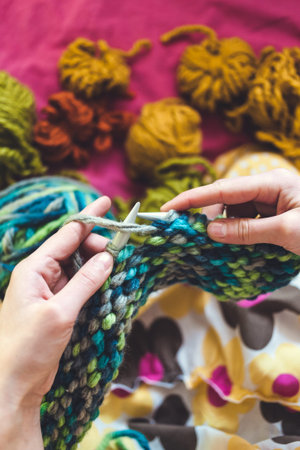 The woman knits. Knitting with knitting needles. Tubes of woolen threads. Multi colored thread. The...