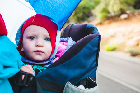 Baby in the backpack. A little boy is traveling with his parents. A trip with a child. Portrait of an infant. Hiking with the baby.の写真素材